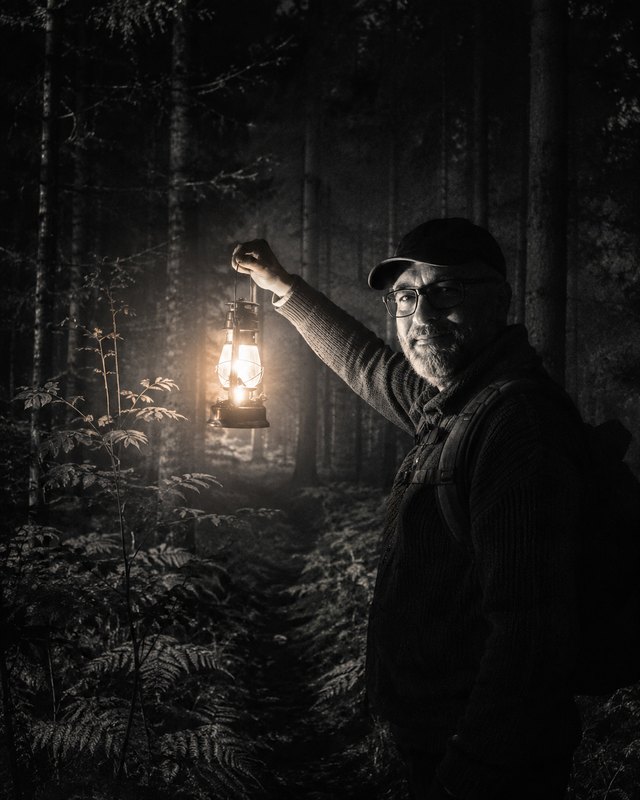 Elias Norren in a dark forest, holding a lit lantern
